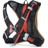 USWE lightweight race hydration pack with black mesh harness, tan reservoir compartment, red hydration tube, and No Dancing Monkey 4-point harness system for mountain biking and gravel racing.